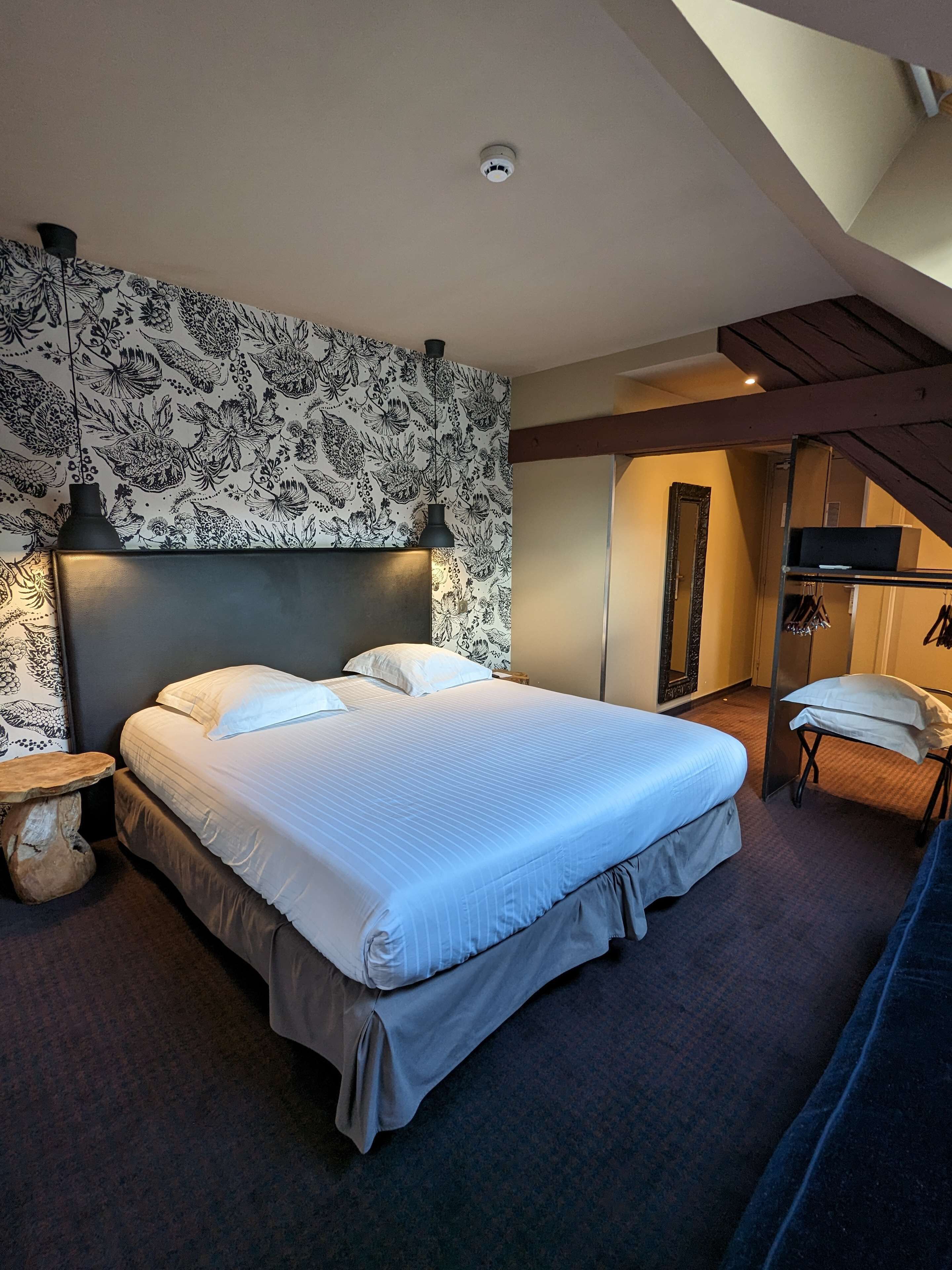 Une chambre moderne avec un grand lit, un mur décoratif, une petite table et un miroir.