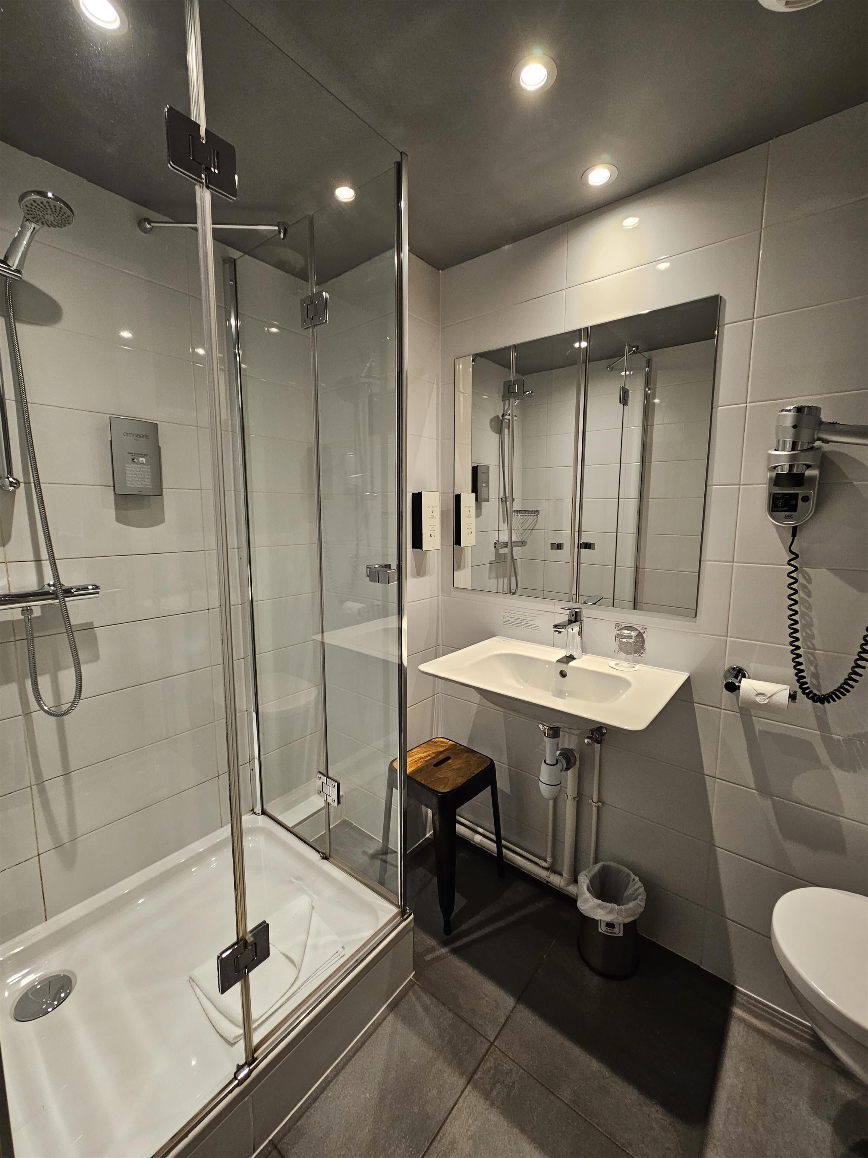 Un baño moderno con ducha de vidrio, lavamanos blanco, espejo y retrete.