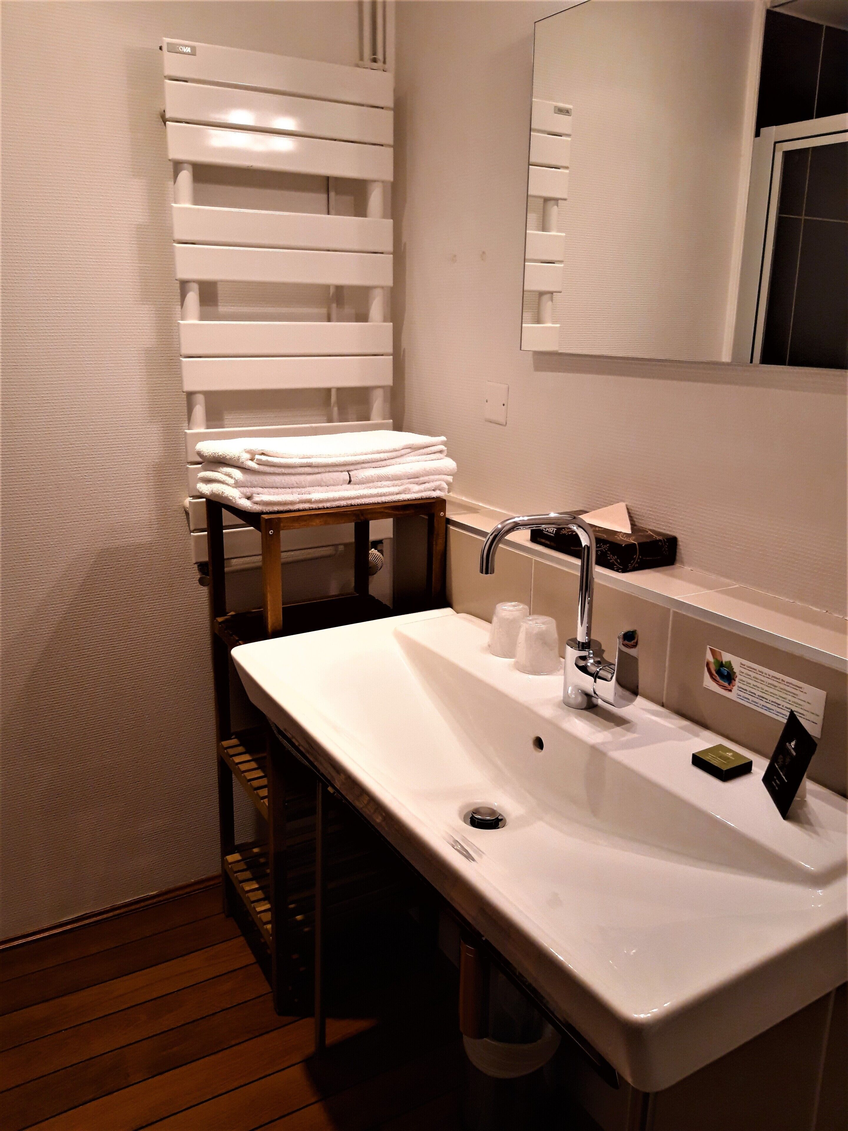 A bathroom with a white sink, a mirror, a towel rack, and a wooden shelf.