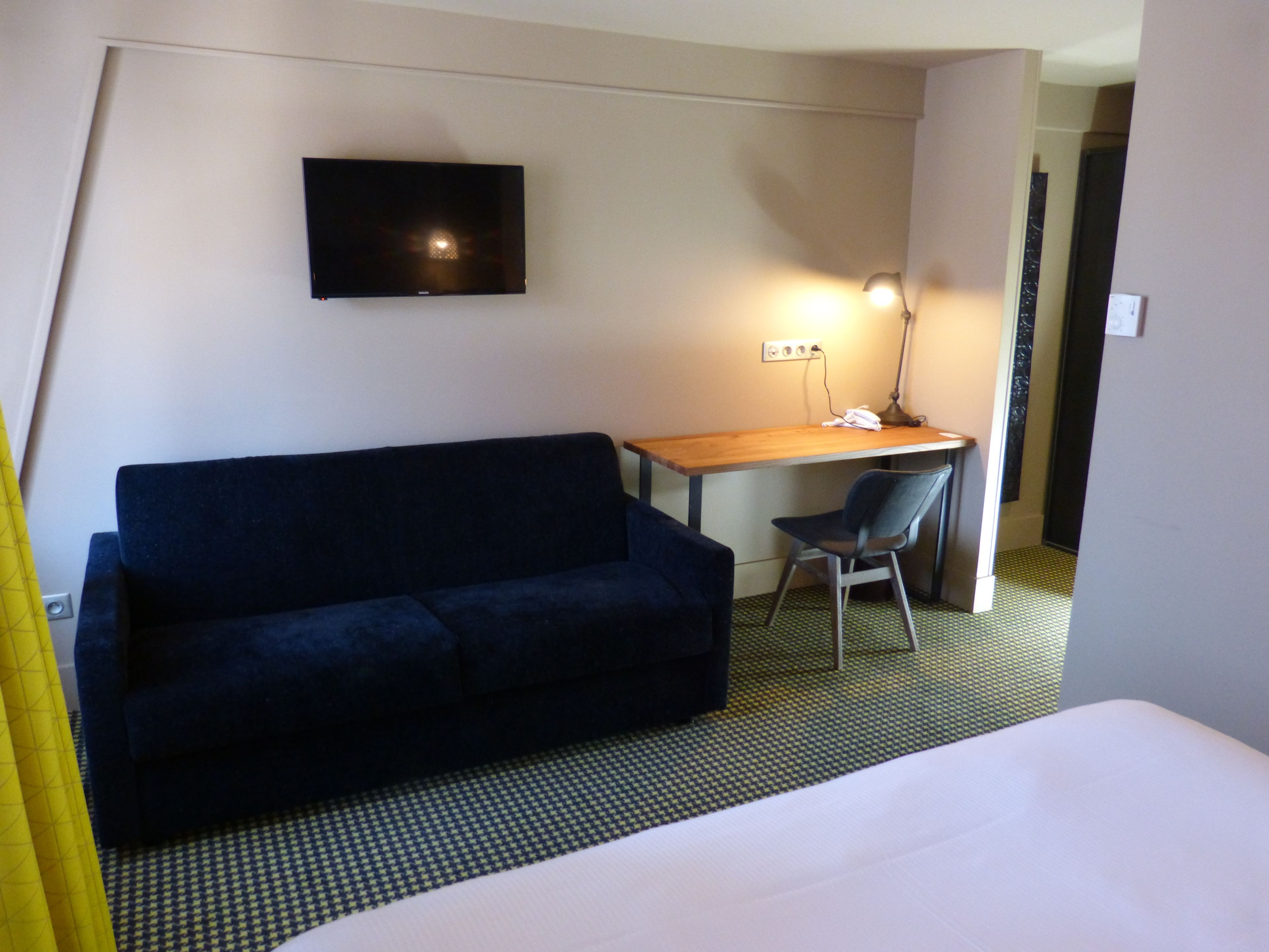 Une chambre d’hôtel avec un lit, un canapé bleu foncé, un bureau avec une chaise, une télévision et une lampe.