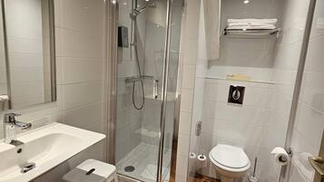 Un baño moderno con ducha envuelta en vidrio, lavabo blanco, inodoro y suelo de madera.