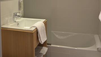 Un baño con tocador de madera, un lavamanos blanco y una bañera.
