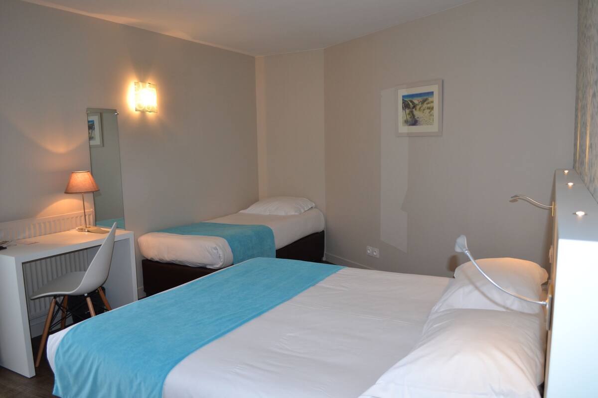 A hotel room with two beds, a desk, a chair, and a lamp.