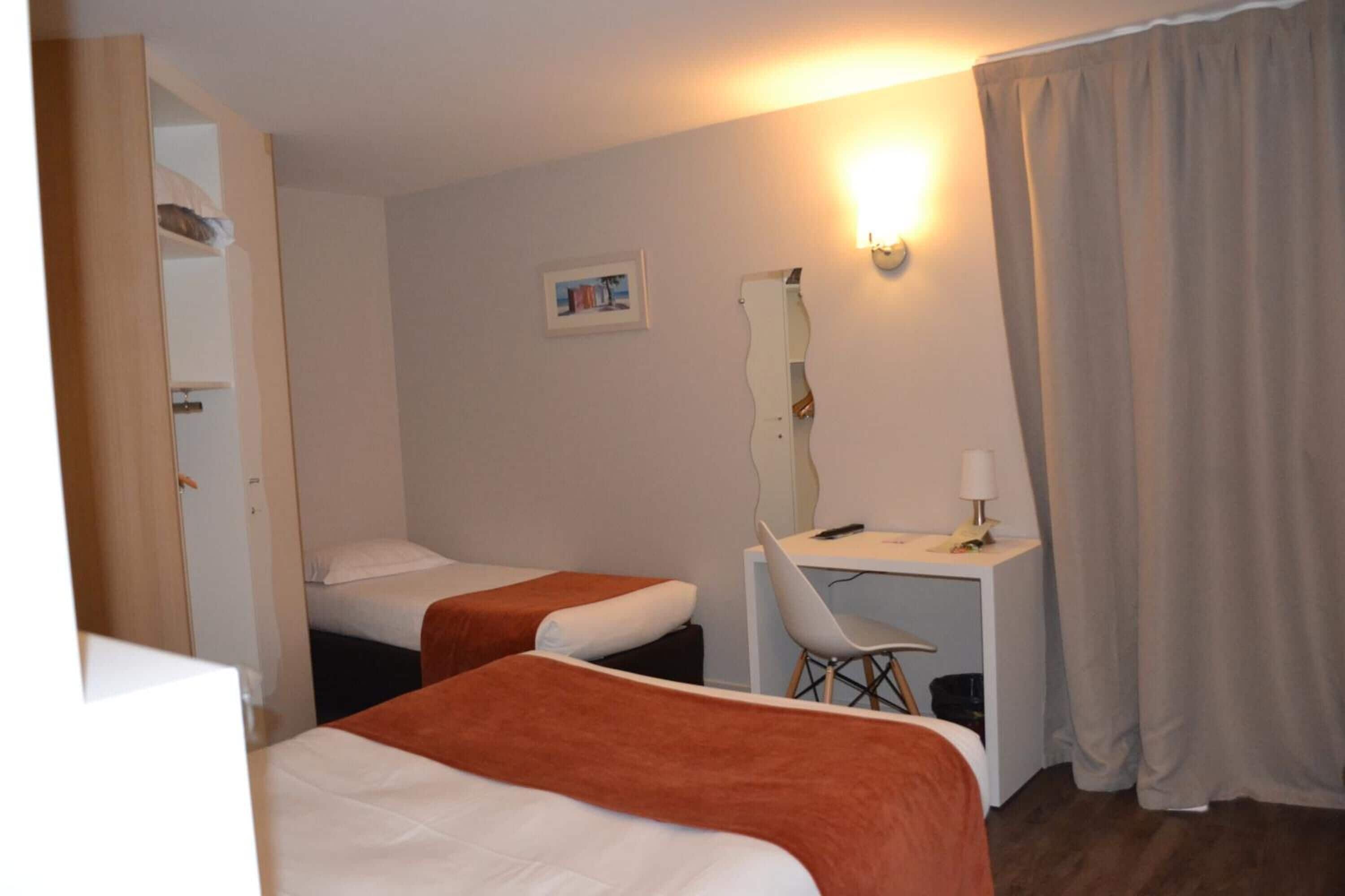 A hotel room with two beds, a desk, a chair, a mirror, and a picture on the wall.
