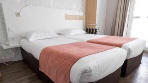 A double bed with white and pink bedding, a bedside table, and a wall-mounted lamp. - Brit Hotel Les Alizés (Pornic)