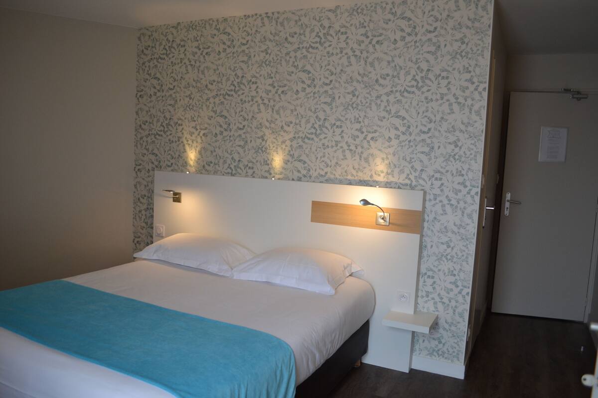 A neatly made bed with a blue blanket, a bedside table, and wall-mounted reading lights.