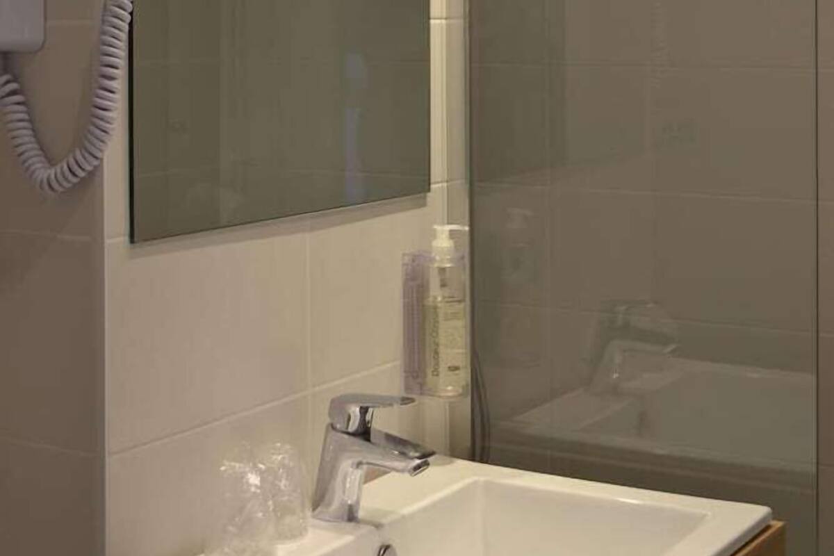 A bathroom with a glass-enclosed shower, a white sink with a mirror above it, and a towel hanging on a hook.