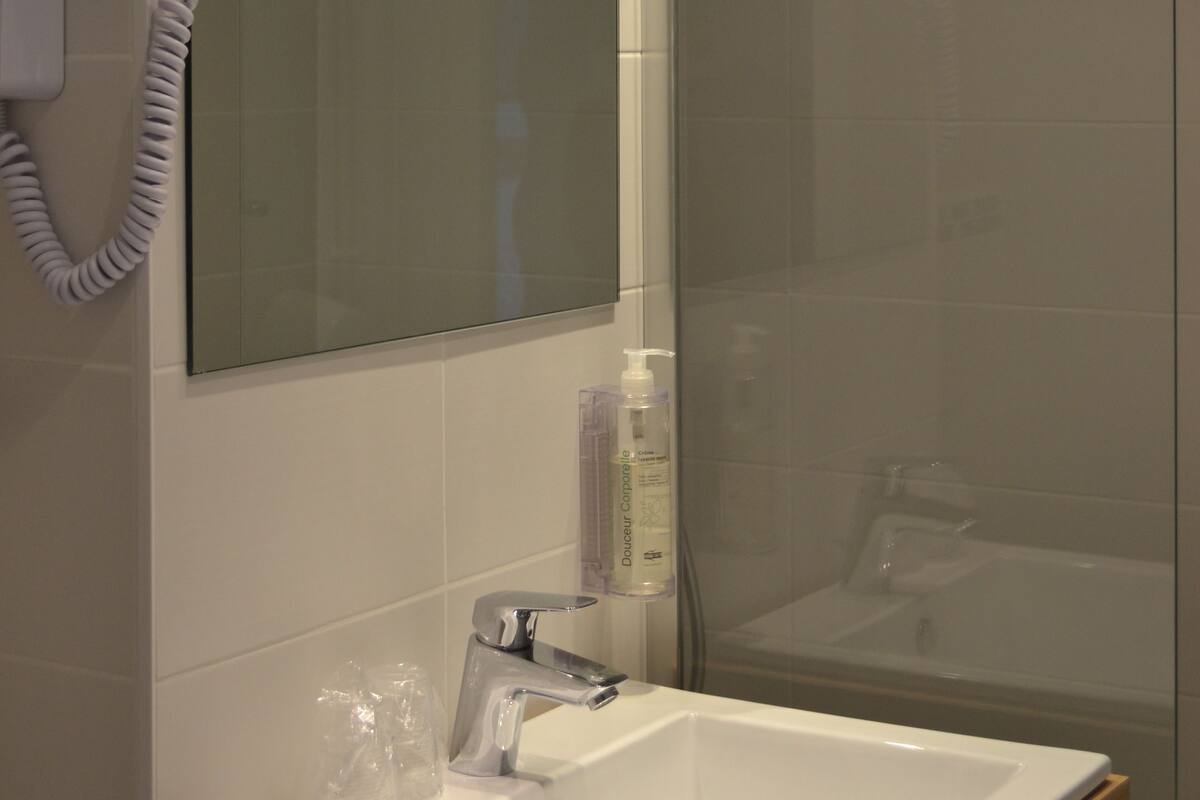 A modern bathroom with a glass shower enclosure, a white sink with a mirror above it, and a towel hanging on a hook.