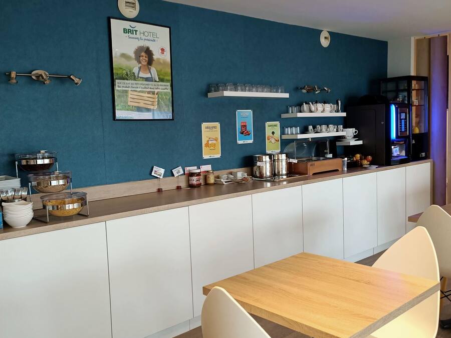 Una cocina moderna con una pared azul decorativa, una cafetera y un comedor con mesa de madera y sillas blancas.