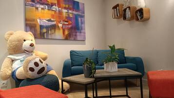 A cozy living area with a large teddy bear, a blue sofa, a coffee table, and a colorful abstract painting on the wall.