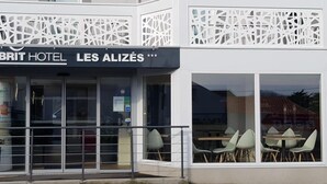 The exterior of the Brit Hotel Les Alizés with a modern facade, large windows, and outdoor seating area. - Brit Hotel Les Alizés (Pornic)