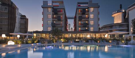 A hotel with a pool, outdoor seating, and a well-lit facade.