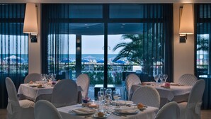 A dining area with tables set for a meal, overlooking a scenic view of the sea and palm trees. - Hotel Orient & Pacific (Jesolo)