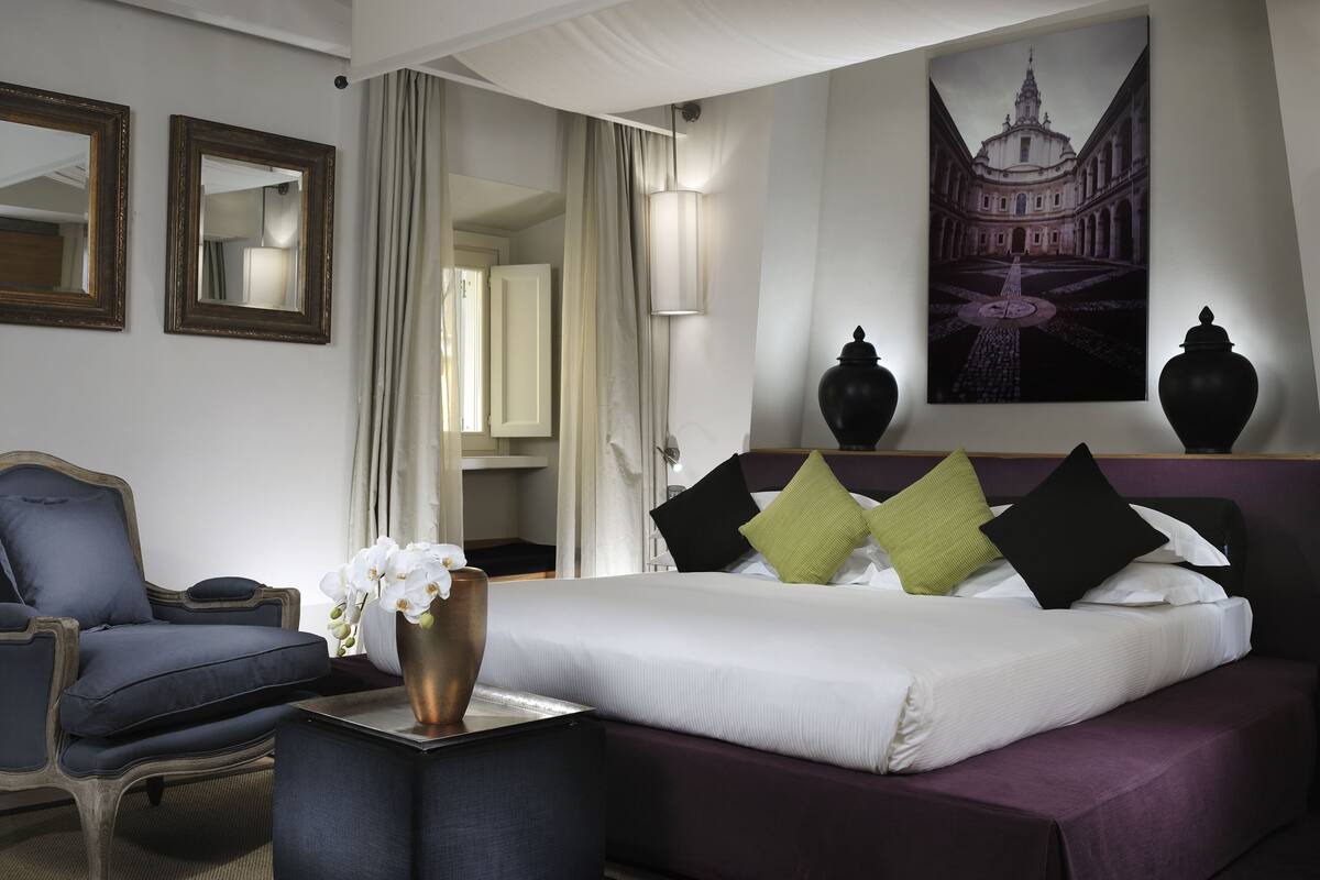 Une chambre d ’hôtel avec un lit, une chaise, un vase de fleurs et un tableau au mur.