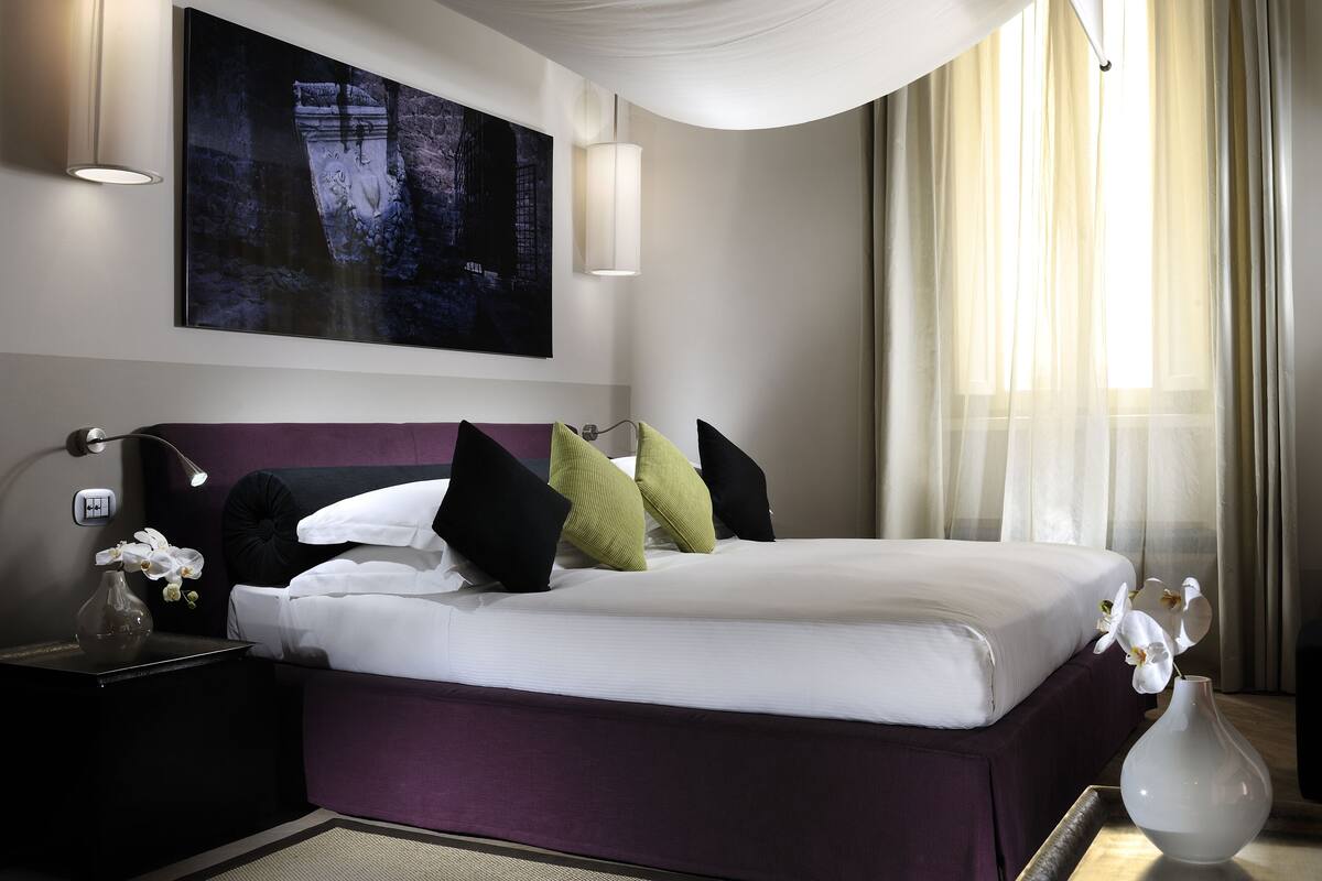 Une chambre d’hôtel moderne avec un grand lit, une table de chevet avec une lampe, un vase de fleurs et un tableau au mur.