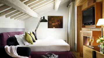 Habitación de hotel con cama, escritorio con lámpara, televisor y un cuadro en la pared.