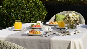 An outdoor dining table with breakfast items, surrounded by greenery and a building in the background. - Mario de Fiori 37 (Rome)