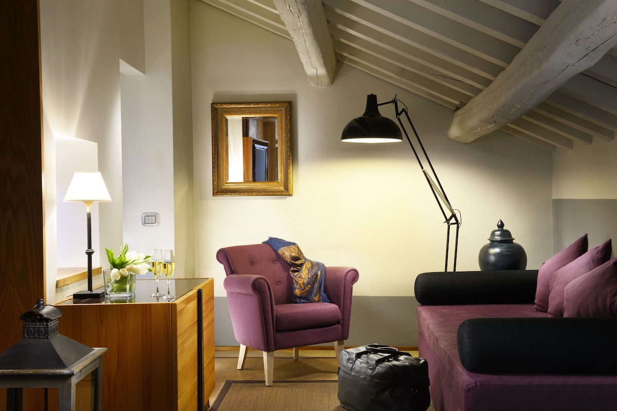 A room with a wooden desk, a purple armchair, a black floor lamp, and a purple sofa.
