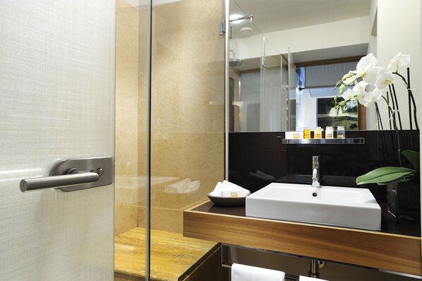 A modern bathroom with a glass shower enclosure, a white sink, and a mirror with a shelf holding toiletries. - Mario de Fiori 37 (Rome)