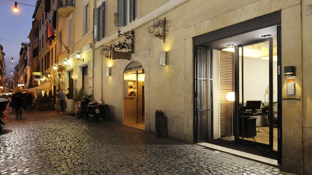 A cobblestone street with a boutique hotel entrance, outdoor seating, and a visible shop. - Mario de Fiori 37 (Rome)