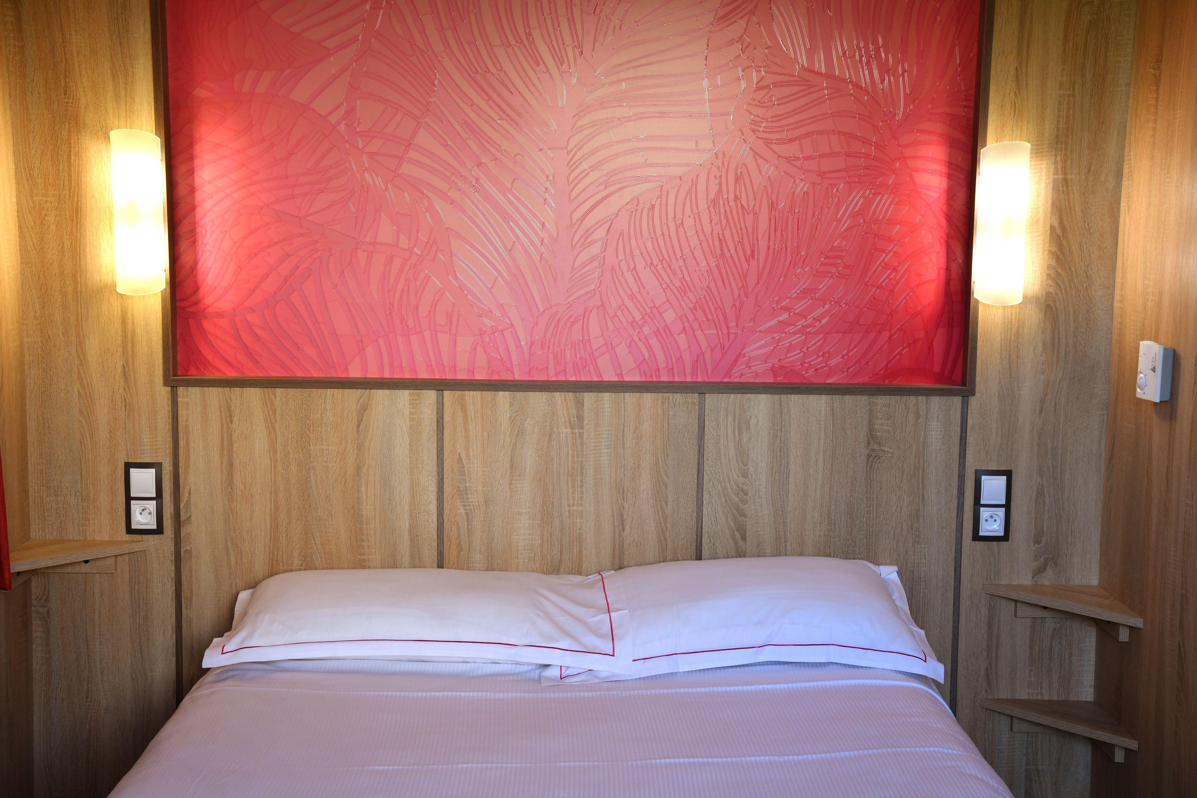Un lit bien fait, avec du linge de lit blanc et un bordure rouge, un grand tableau abstrait rouge accroché au mur et des lambris en bois.