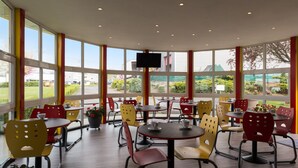 Un restaurante con mesas y sillas redondas, ventanas amplias y un televisor de pantalla plana.