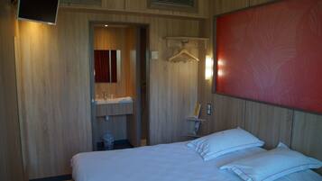 A hotel room with a bed, a mirror, a wall-mounted TV, a red abstract painting, and a wooden panel wall.