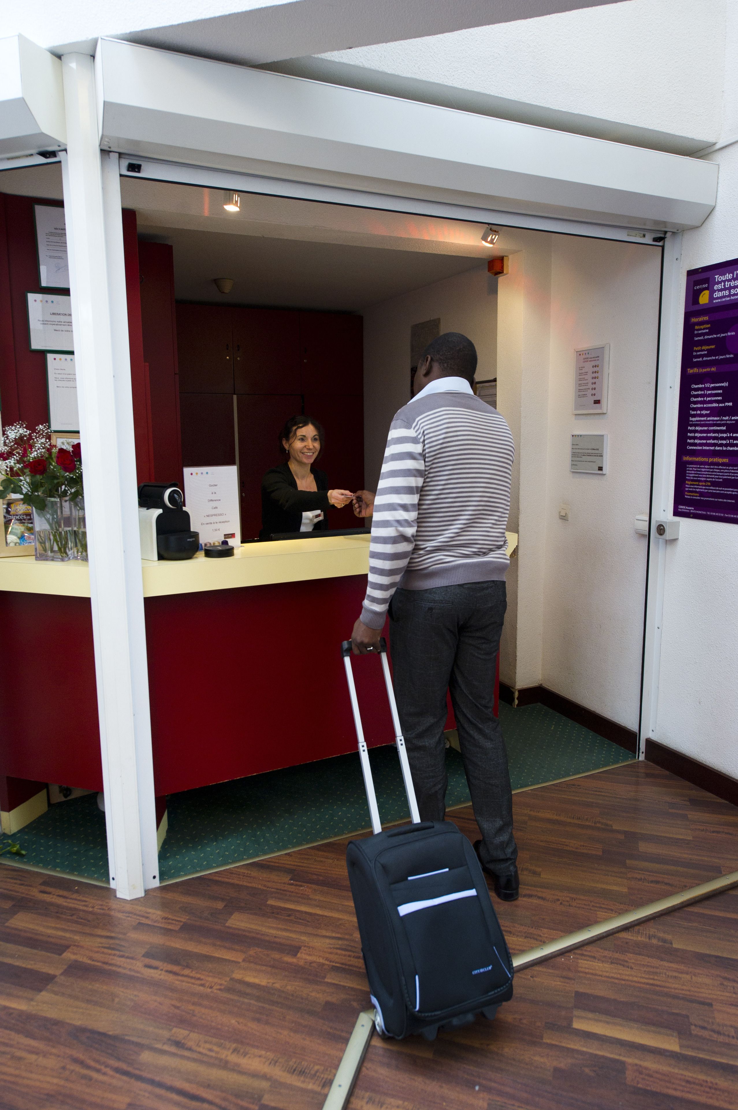 A hotel reception area with a counter, a receptionist, and a guest with a suitcase.