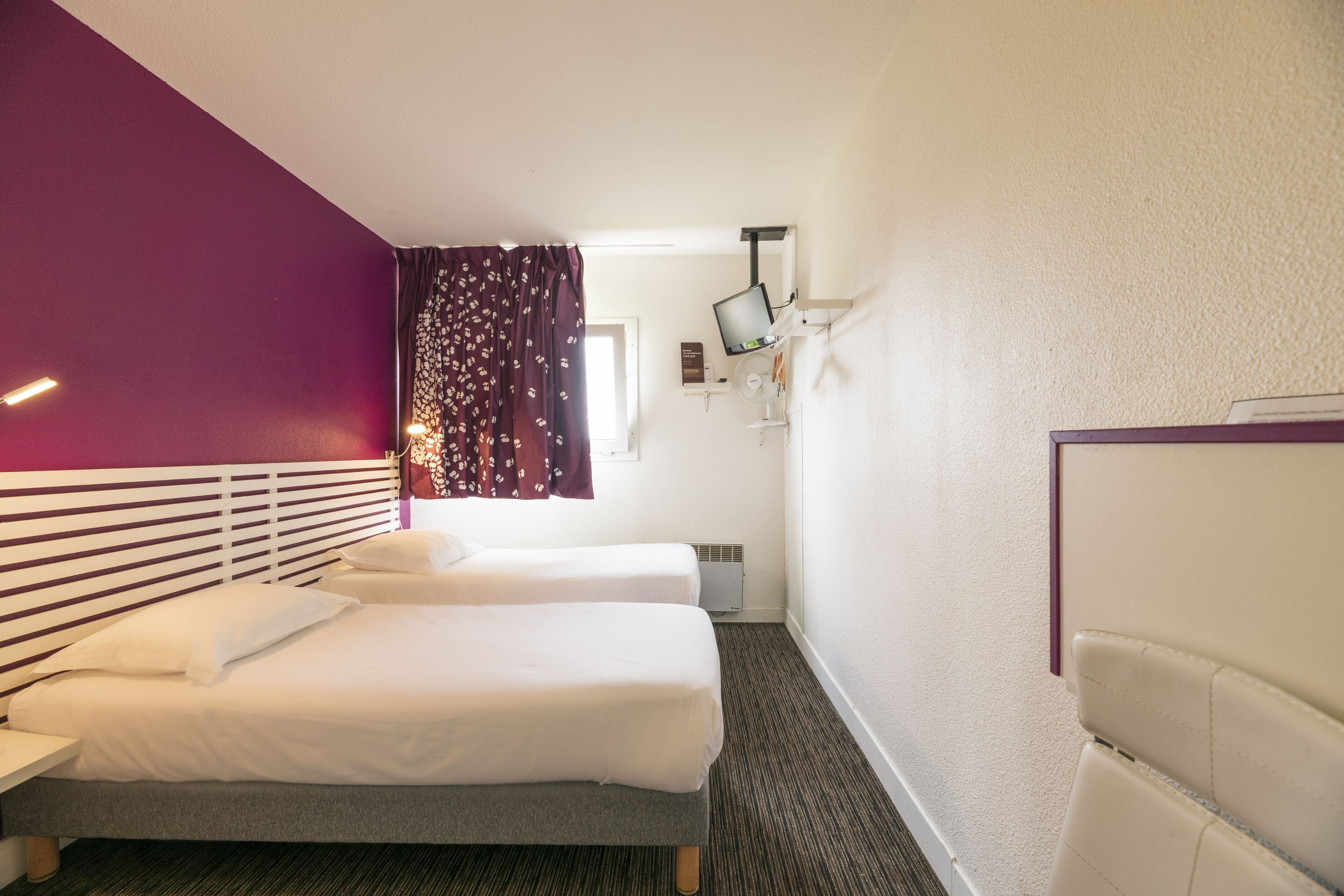 Ein Hotelzimmer mit zwei Betten, einem Flachbildfernseher, einem Schreibtisch und einem Fenster mit Vorhängen.