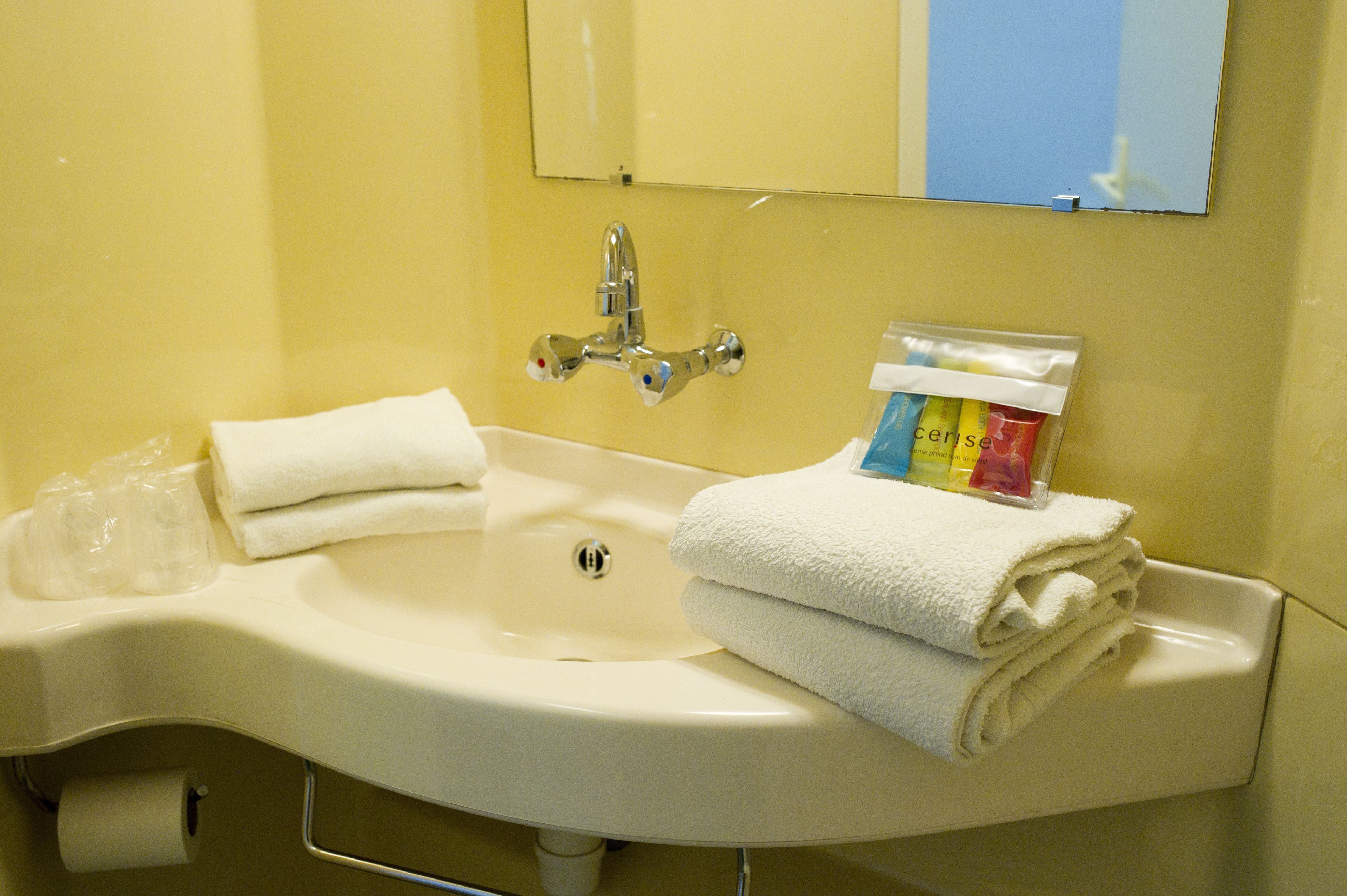 A hotel bathroom sink with a mirror, a towel dispenser, and a toilet paper holder.