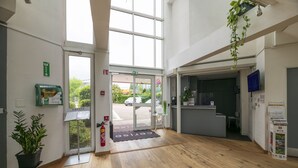 Un vestíbulo de hotel con piso de madera, una recepción, un extintor, una planta verde y un letrero que indica zona de lavado de autos.