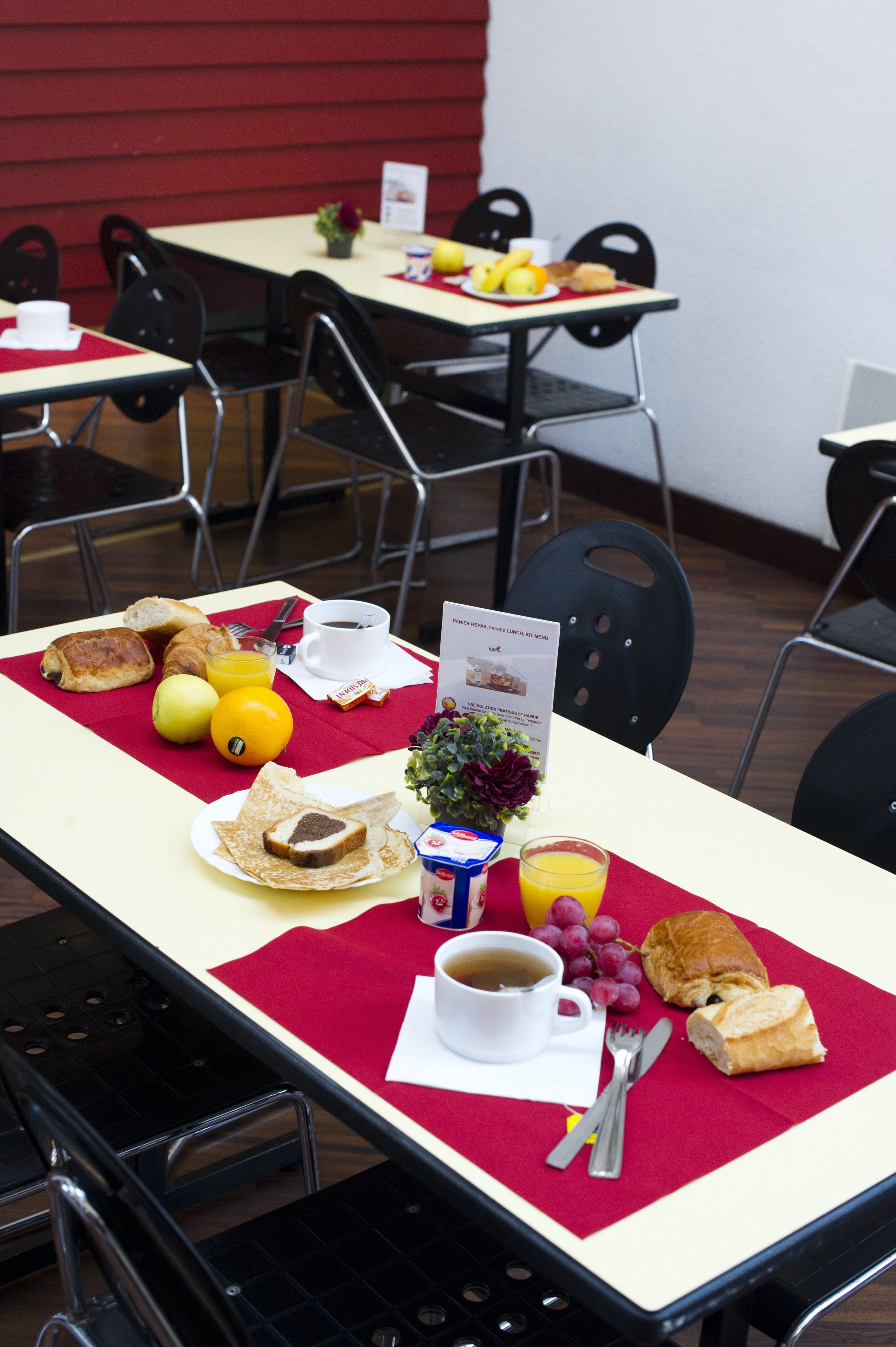 Disposição para o pequeno-almoço com croissants, frutas e bebidas sobre uma mesa com um jogo americano vermelho.