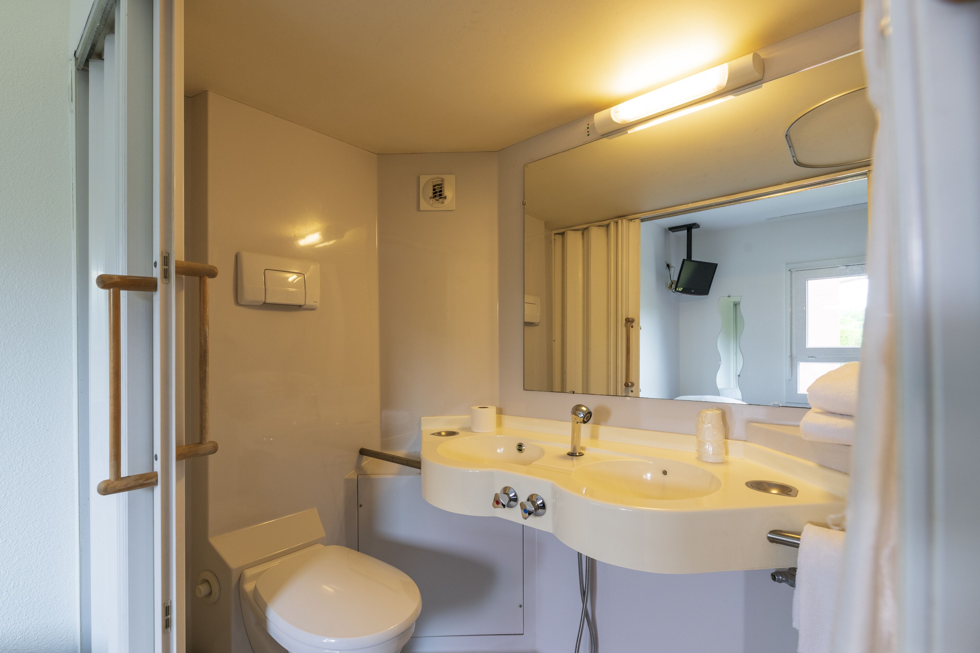 A compact bathroom with a white toilet, a sink with a mirror above it, and a towel rack.