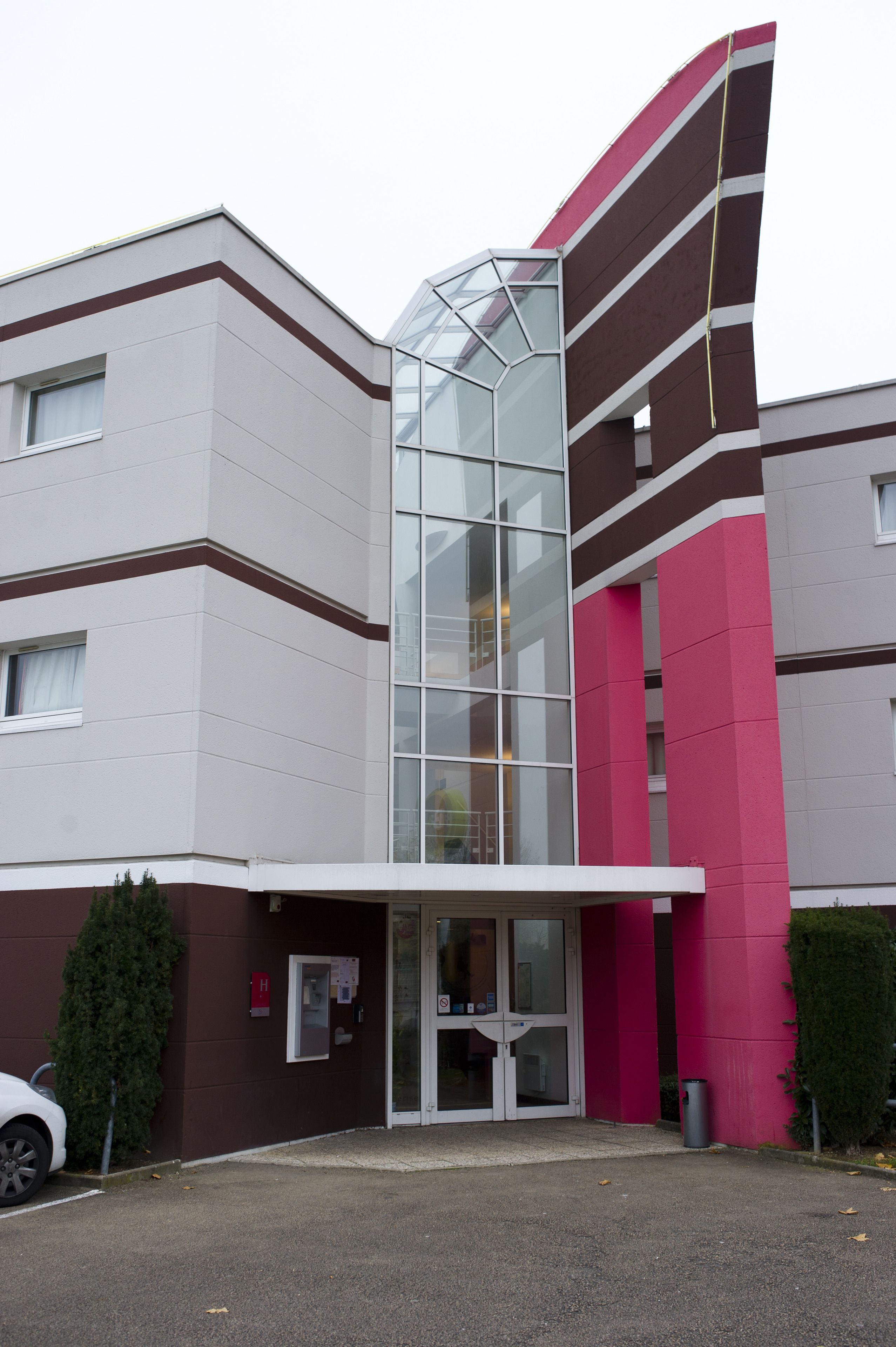 A modern building with a glass entrance and a parking area in front.