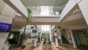 Un interior moderno con un espacio central abierto, una escalera y un balcón con plantas.