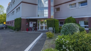 Un edificio moderno con un atrio de cristal, un estacionamiento y una pequeña zona de estar al aire libre.