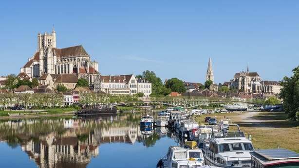 Una catedral histórica con una gran torre, un río con barcos y un puente que conecta dos partes de la ciudad.