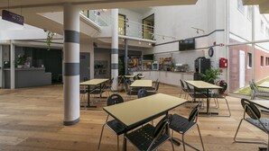 Un espacio interior moderno con varias mesas y sillas, una zona de cocina y una escalera que lleva a un nivel superior.
