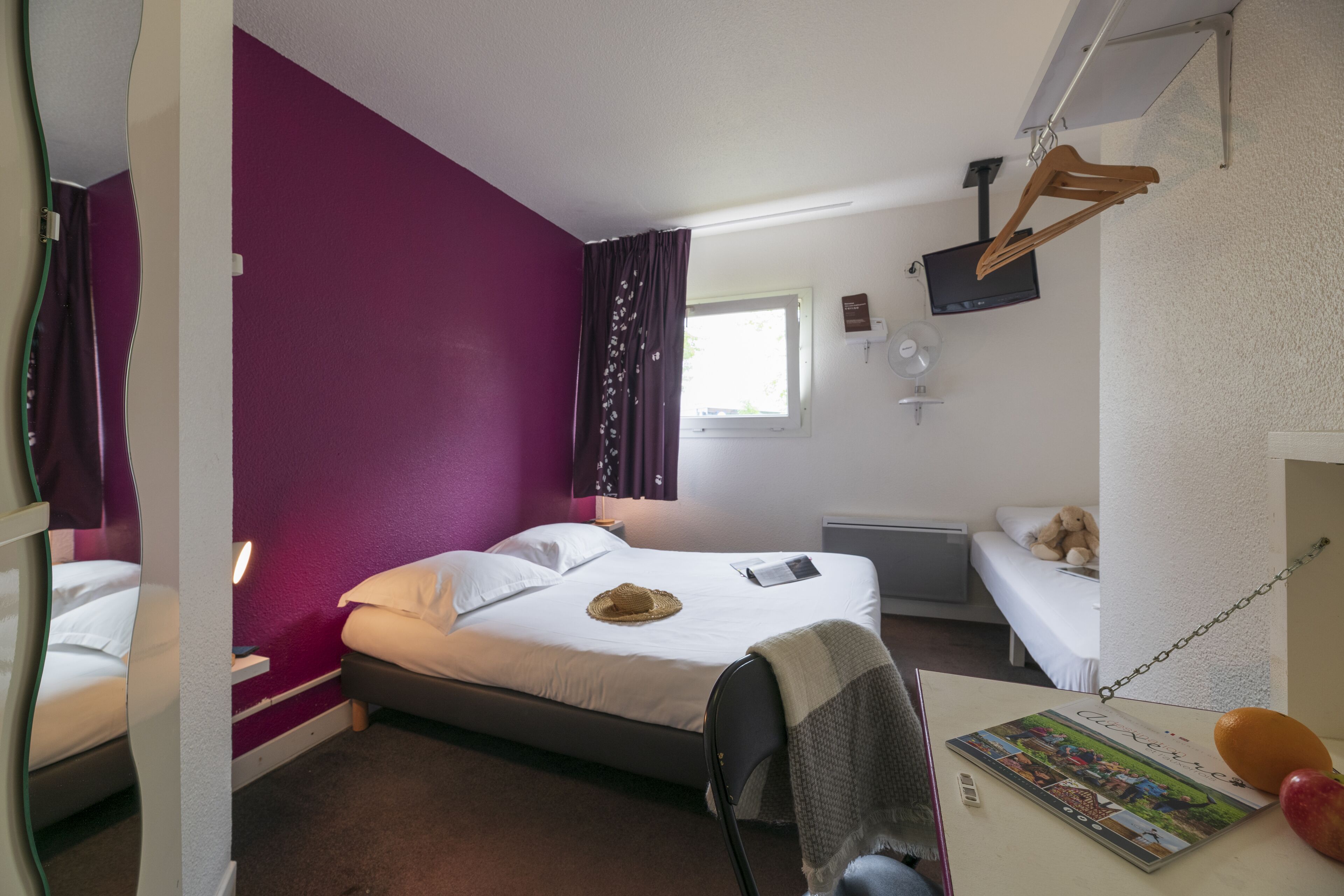 A hotel room with a bed, a desk, a chair, a window, and a television mounted on the wall.