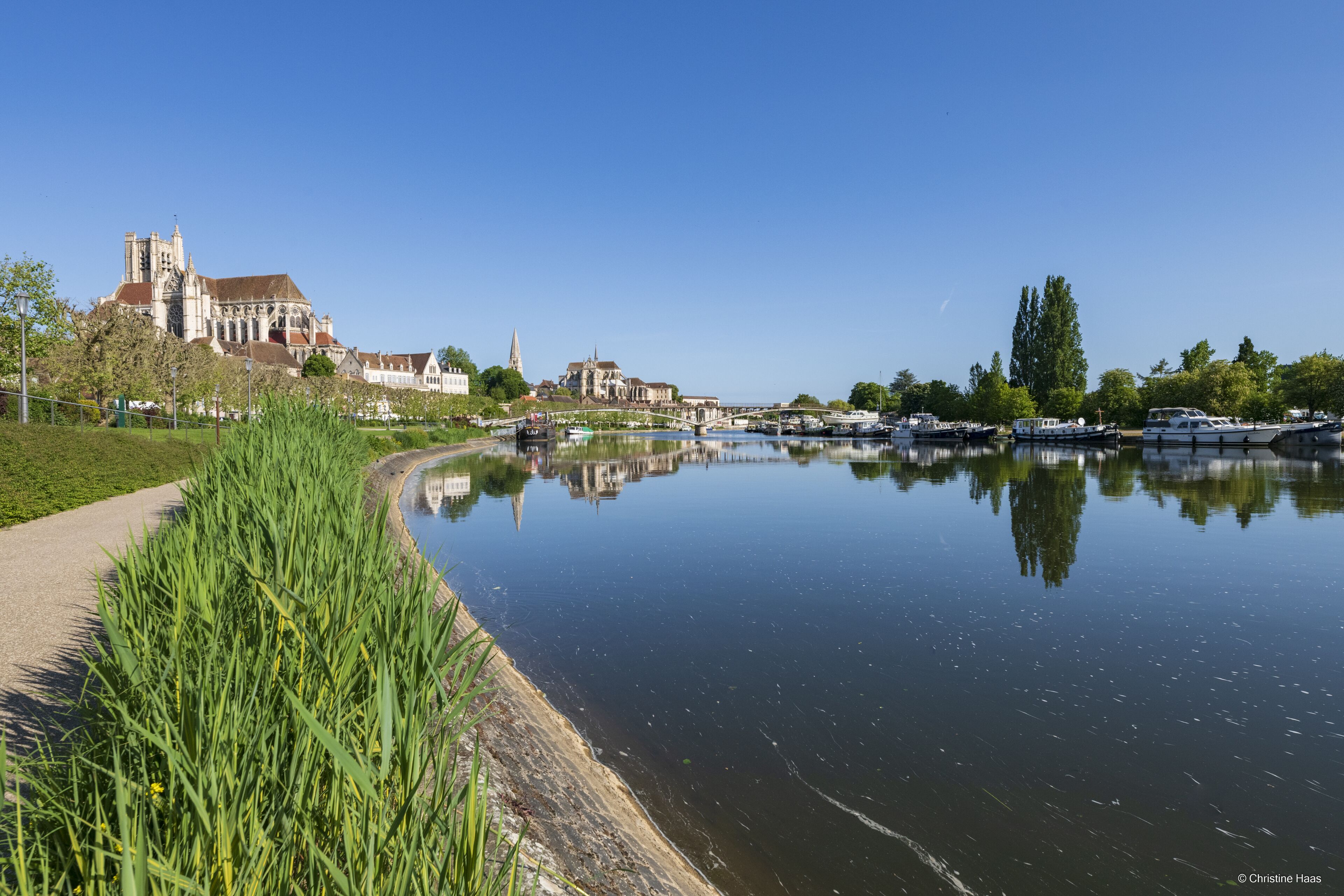 Une rivière où l’on peut voir des bateaux, un sentier et des bâtiments, dont une église imposante.