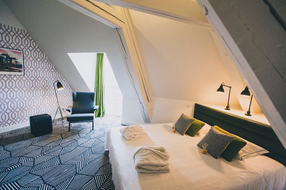 Une pièce triangulaire comprenant un lit, une chaise, un bureau et une lampe.
