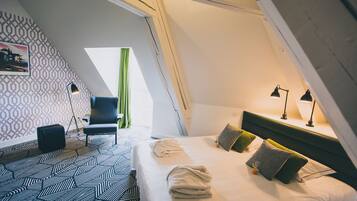 A room with a sloped ceiling, a bed with pillows, a chair, a desk, and a lamp.