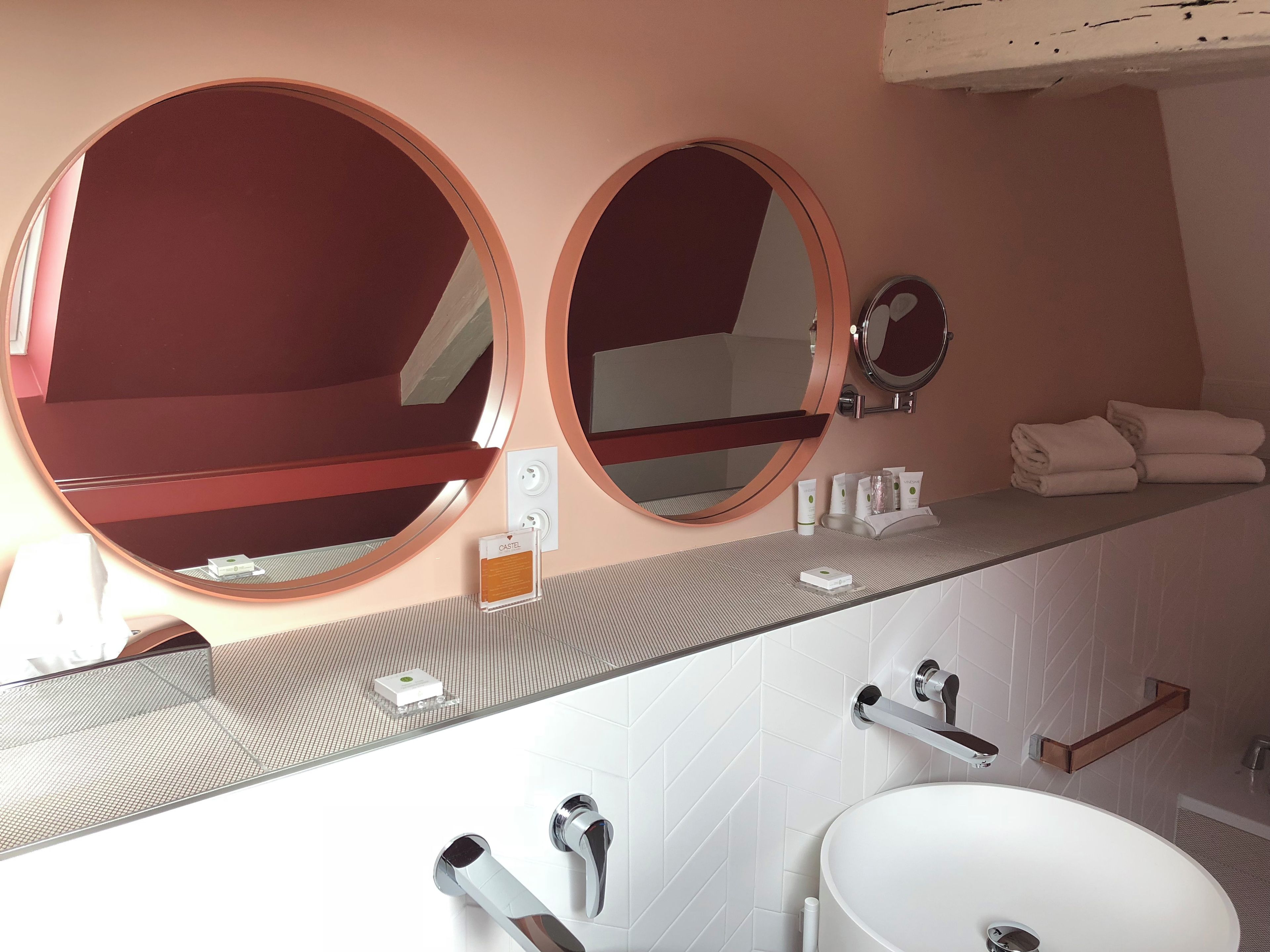 A bathroom with two round mirrors, a white sink, and a towel rack.