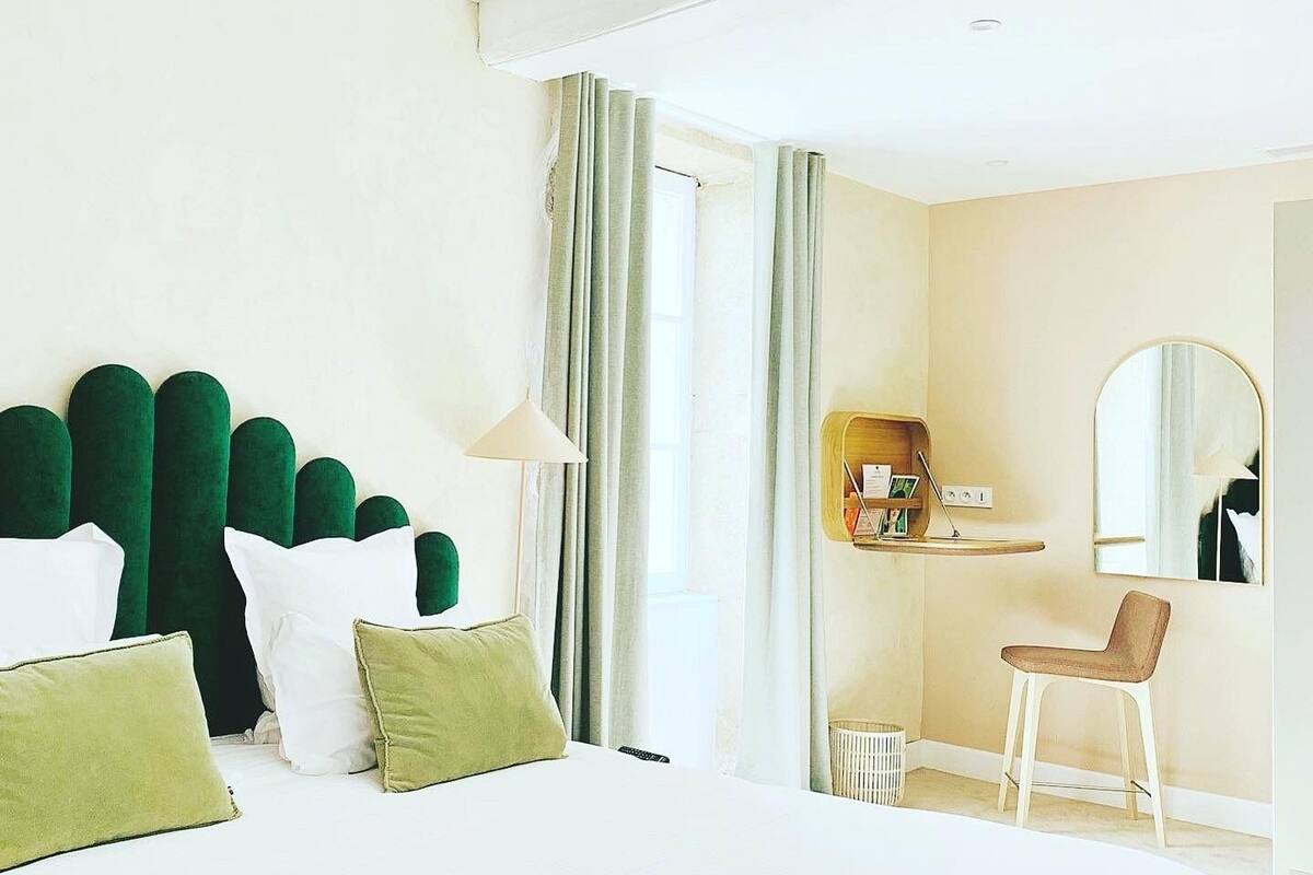Hotellihuone, jossa on suuri sänky, työpöytä tuolilla, peili ja ikkuna, jossa on verhot.