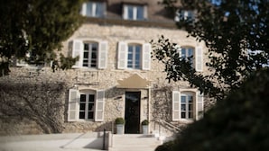 Un edificio de piedra con una entrada central, varias ventanas con contraventanas y una escalera que conduce a la entrada.