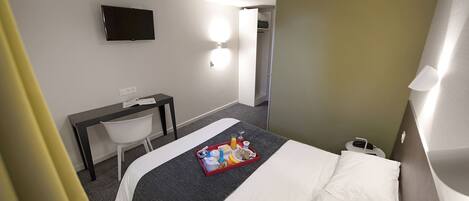 Une chambre d’hôtel équipée d’un lit, d’un bureau, d’une chaise, d’une télévision et d’un plateau de petit-déjeuner.