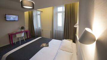 A hotel room with a bed, a desk, a chair, a TV, and a window with curtains.