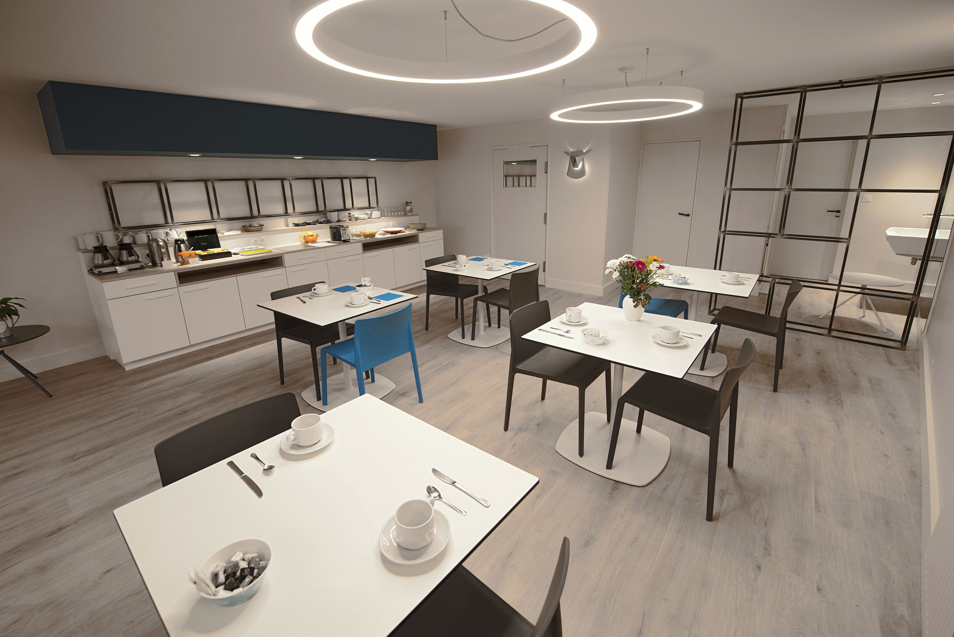 A modern kitchen with white cabinets, a blue accent wall, and a dining area with white tables and chairs.
