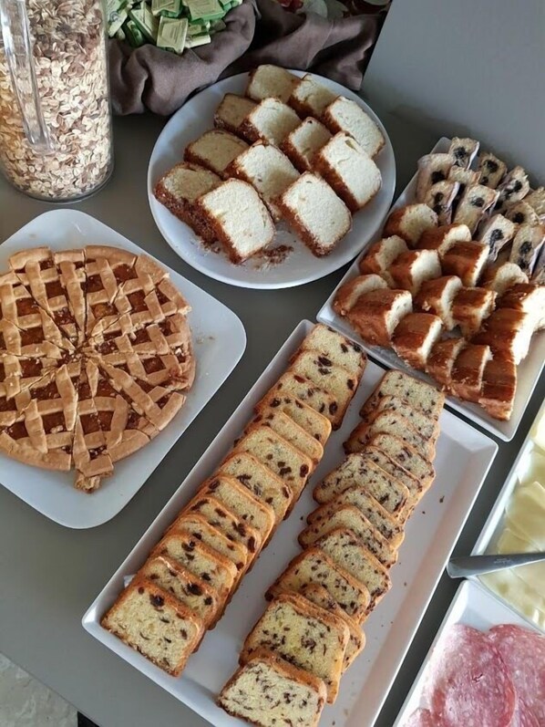 Variedad de pan y pasteles sobre una mesa, incluyendo una tarta con costra enrejada, rebanadas de pan blanco y un pan de pasas.