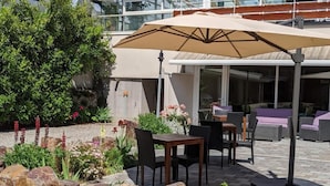 An outdoor patio area with stone seating, a table, and an umbrella. - Hôtel Régina (La Bourboule)